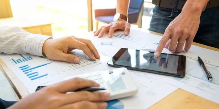 Hands reviewing printed financial charts and a tablet across a desk