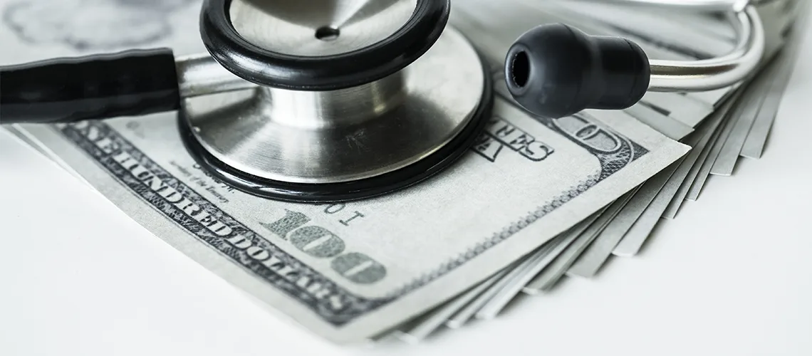 A stethoscope resting on a fan of hundred-dollar bills