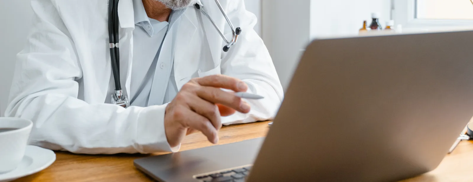 A clinician working at a laptop with a cup of coffee